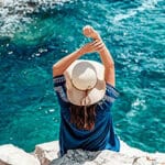 Mujer de espaldas disfrutando de la vista del mar sobre unas rocas, con los brazos alzados