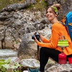 Mujer sentada a la orilla de un rio con una cámara en mano