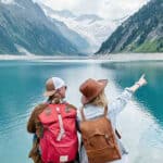 Pareja de turistas de espaldas a la orilla de un lago entre las montañas